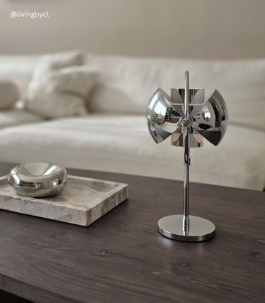 Lampe à poser design chromée sur une table en bois devant un canapé clair.